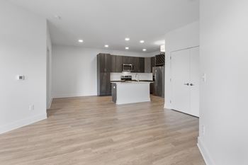 An empty living room and kitchen with white walls and wood flooring